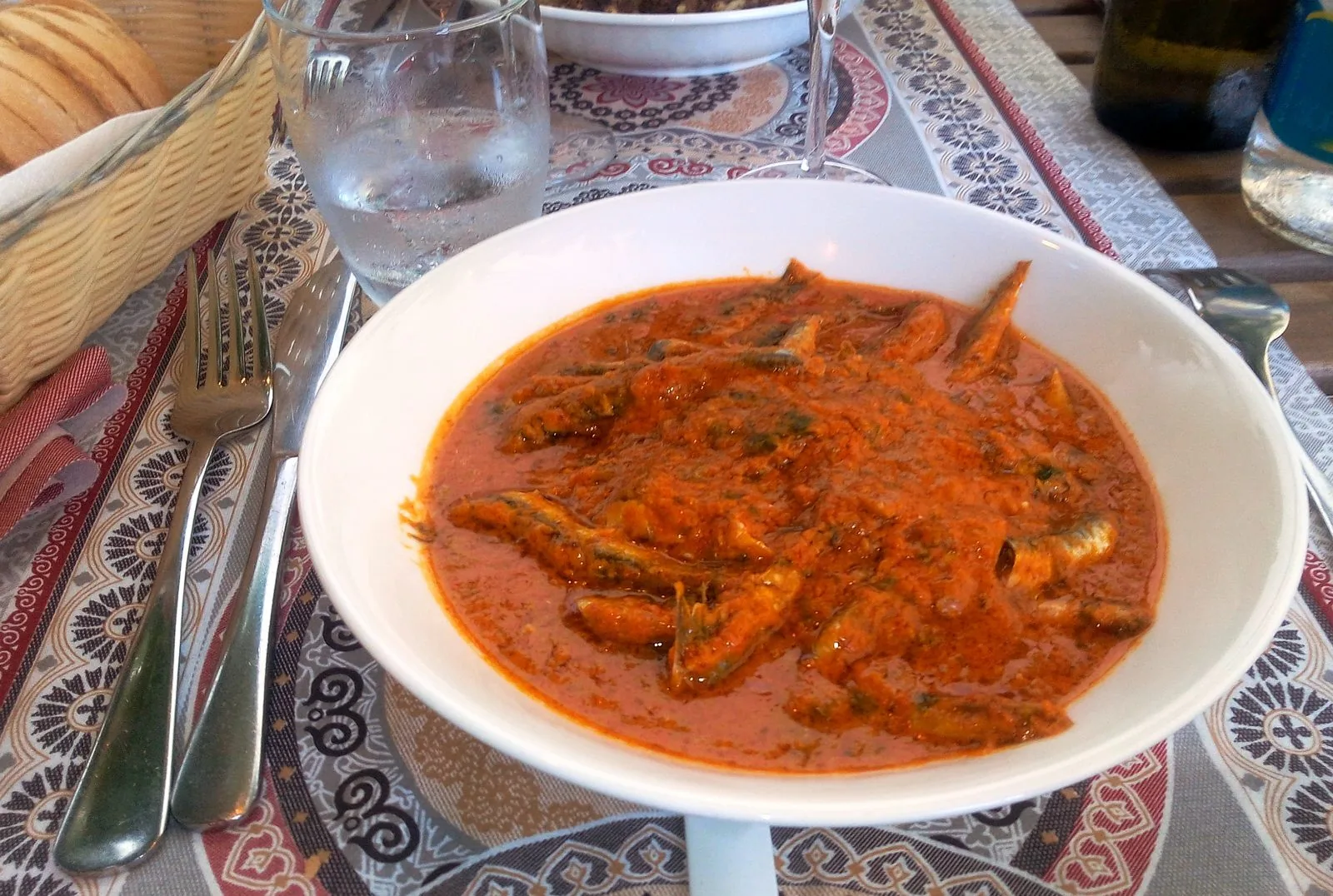 Piatto di bagnun, acciughe cotte in sugo di pomodoro, servito su una tavola apparecchiata