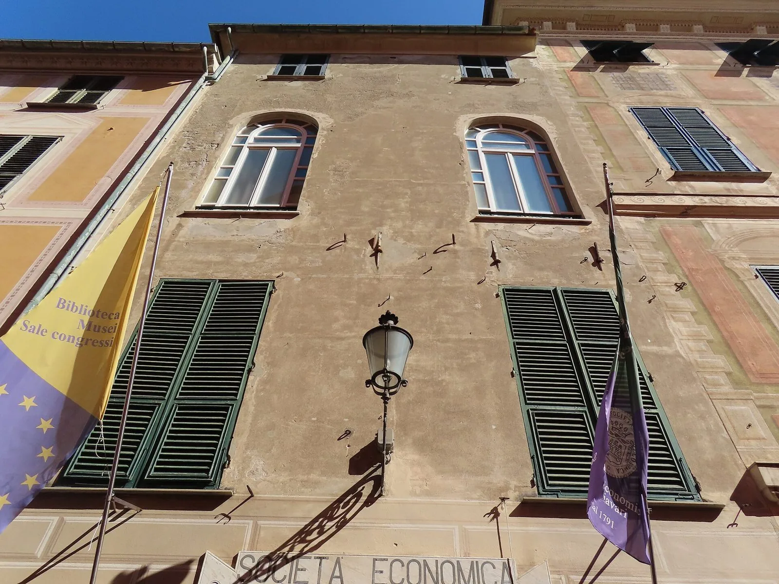 Facciata della sede della Società Economica di Chiavari con persiane verdi, lampione in ferro battuto e bandiere